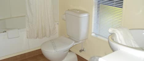Une salle de bain équipée de toilettes, d’une baignoire et d’une fenêtre avec des stores.
