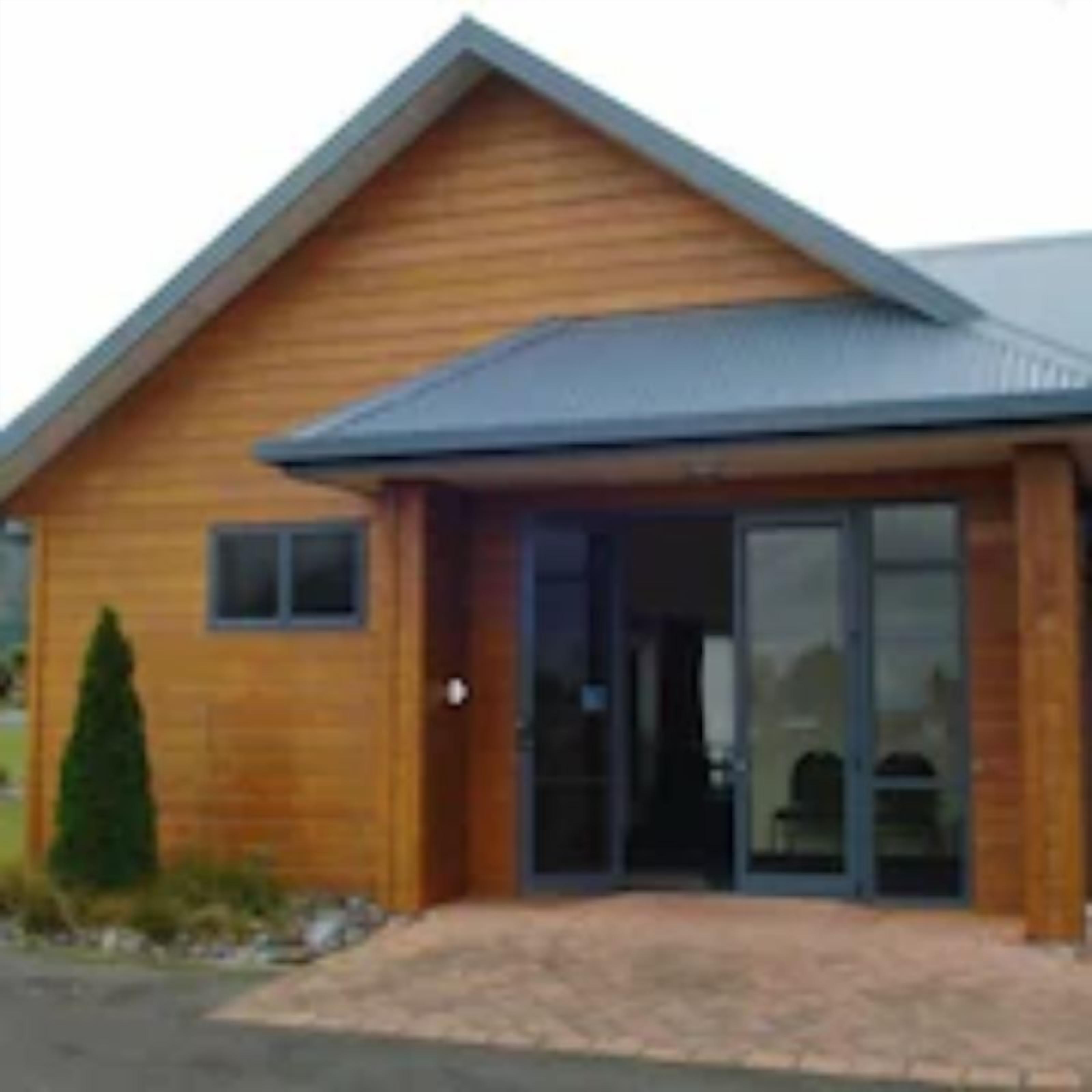 A wooden building with a sloped roof and a large glass door entrance.