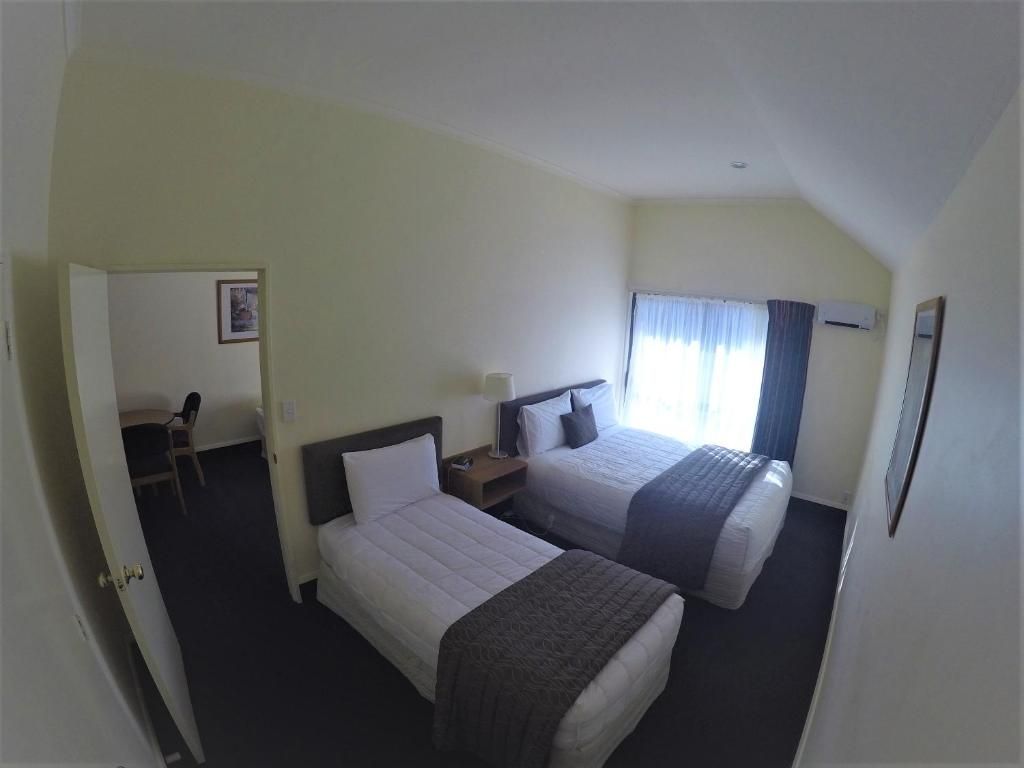 A hotel room with two beds, a desk, a chair, and a window with curtains.