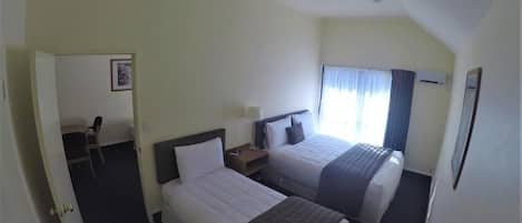 A hotel room with two beds, a desk, a chair, and a window with curtains.