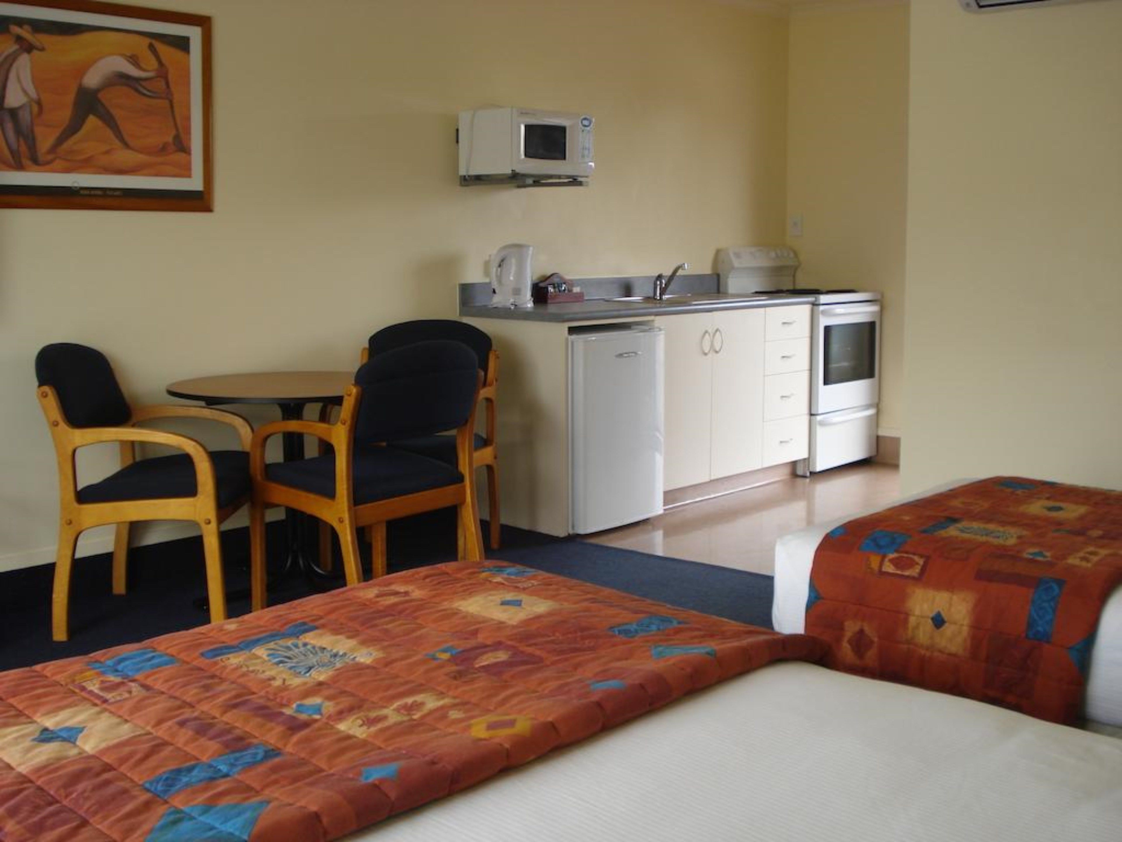 Habitación de hotel con dos camas individuales, un pequeño rincón de cocina, una mesa de comedor con sillas y un cuadro en la pared.