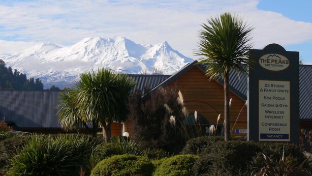 Un hotel llamado "The Peaks Motor Inn" con un letrero que enumera comodidades como habitaciones tipo estudio y familiares, piscinas termales, sauna y gimnasio, internet inalámbrico y una sala de conferencias.