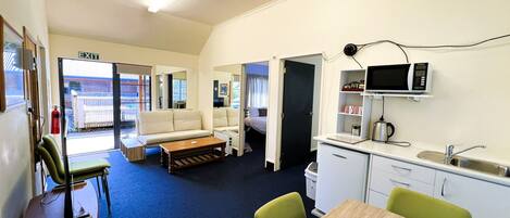 Une chambre d’hôtel compacte dotée d’une kitchenette, d’un canapé, d’une table à manger et offrant une vue sur l’extérieur.