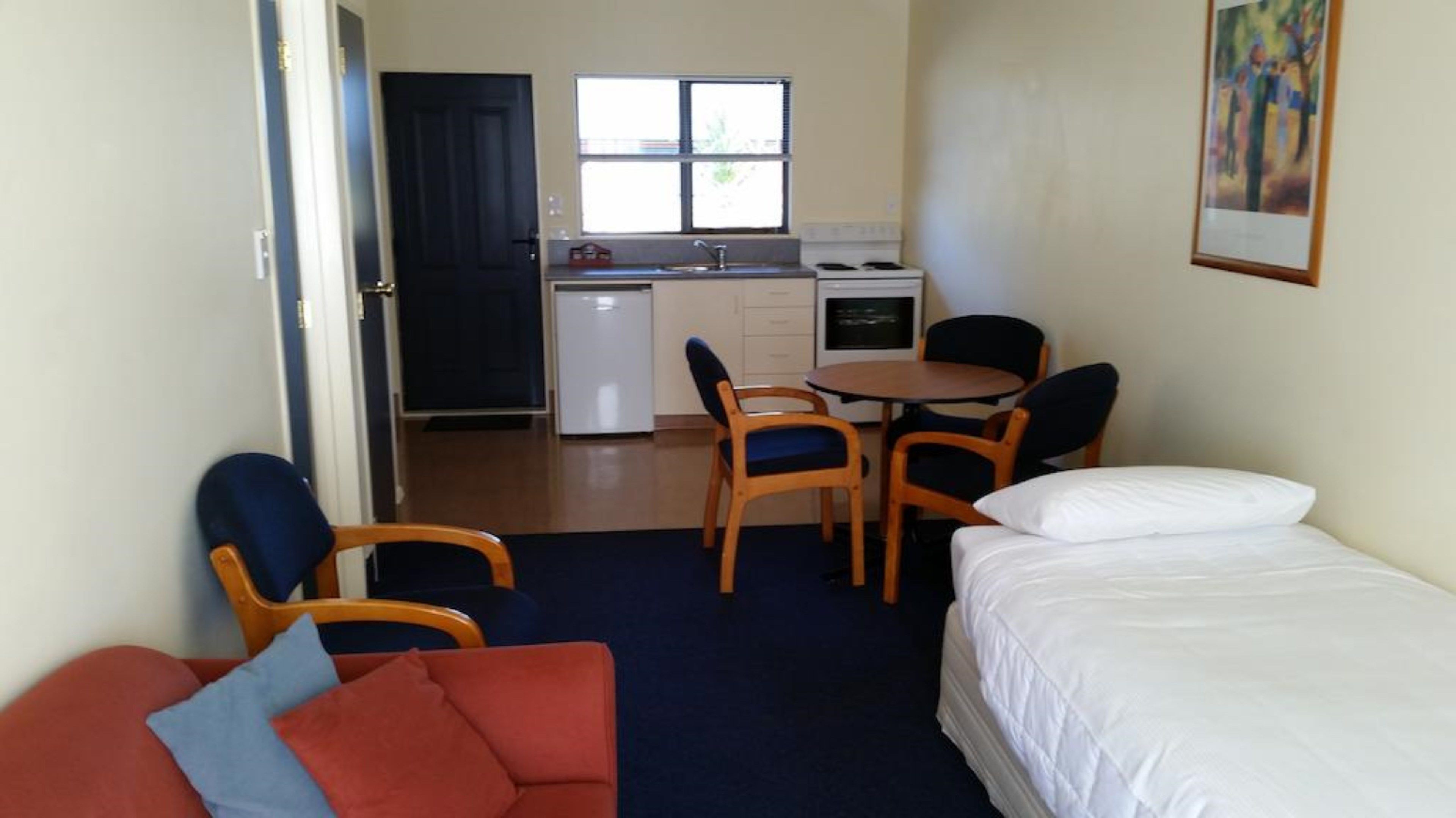 Ein kompaktes Hotelzimmer mit Bett, einer kleinen Sitzecke, einem Esstisch mit Stühlen, einer Küchenzeile und einem Fenster.