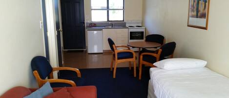 Een kleine hotelkamer met een bed, een klein zitaapje, een eettafel met stoelen, een kitchenette en een raam.
