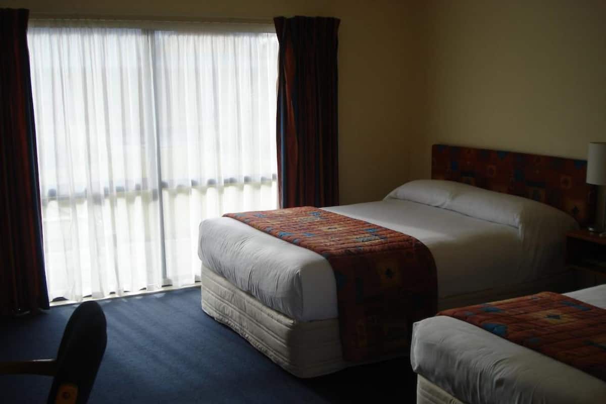 Quarto de hotel com duas camas, uma cadeira e vista para uma varanda.