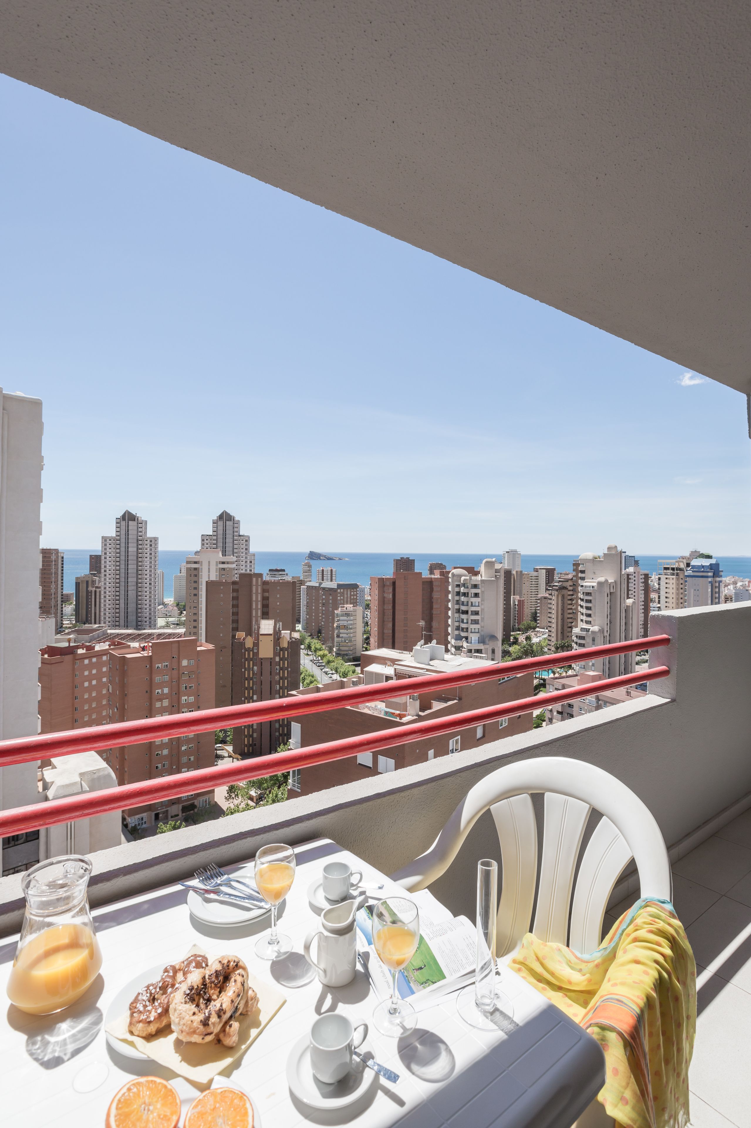 Un balcon avec une table préparée pour le petit-déjeuner, offrant une vue sur le paysage urbain et la mer.