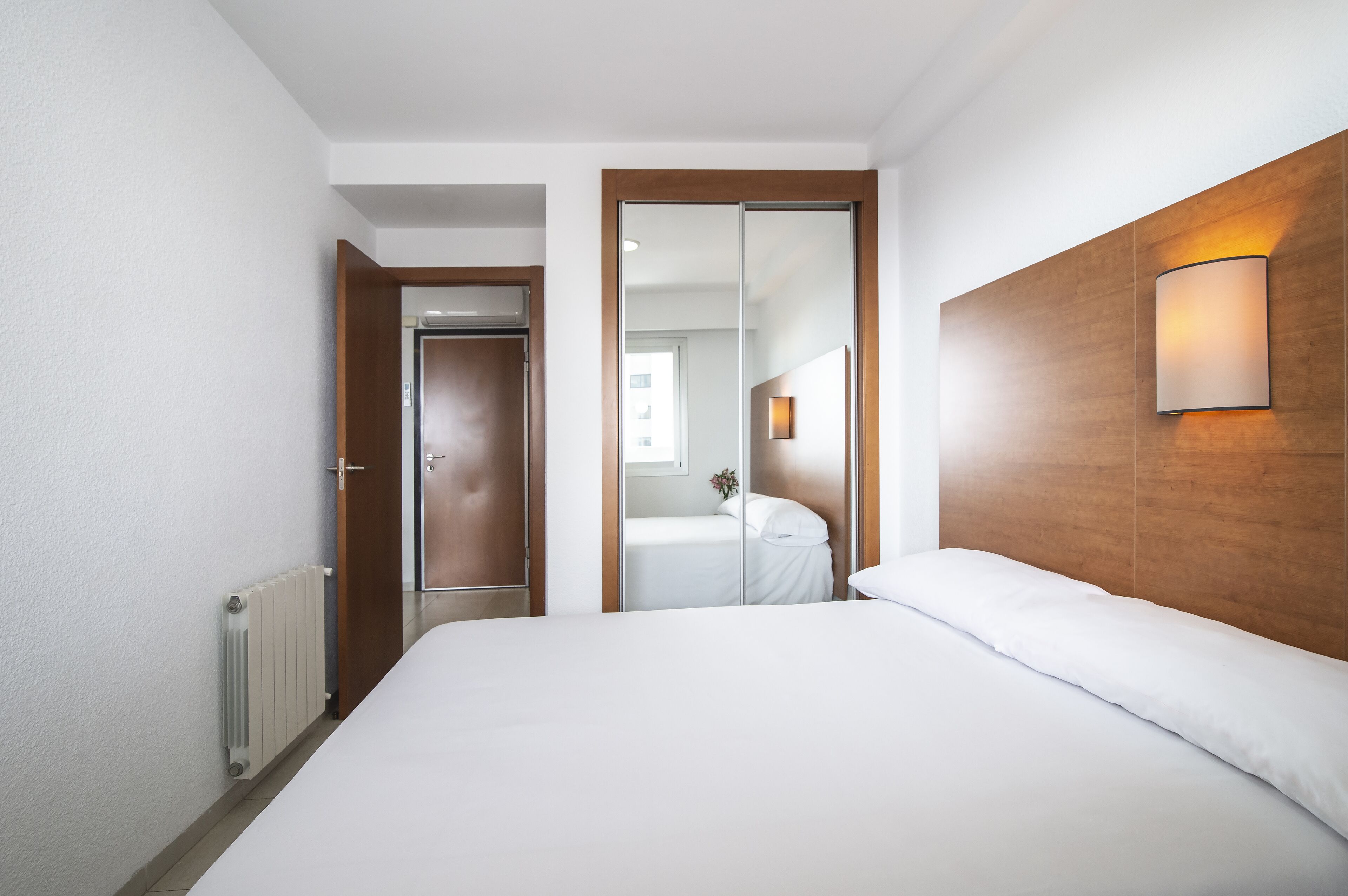 Een hotelkamer met een groot bed, een houten hoofdbord, een spiegel en een wandlamp.