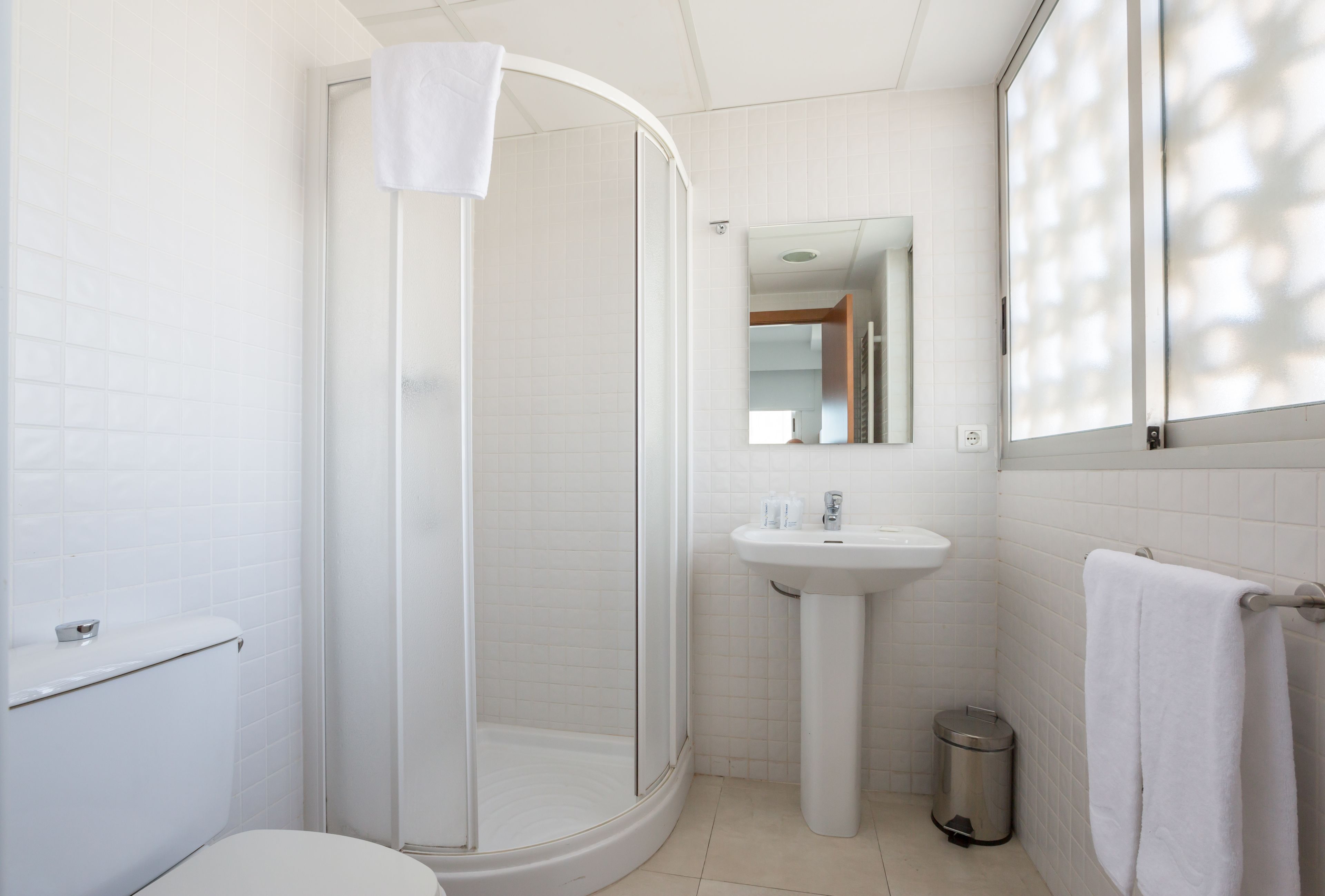 A modern bathroom with a glass-enclosed shower, a pedestal sink, and a toilet.