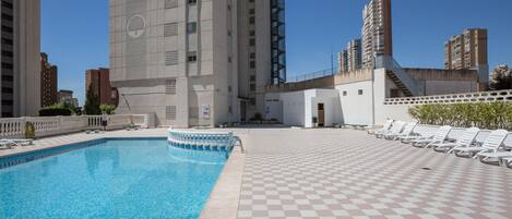 Uma área de piscina no terraço com piso xadrez, uma piscina e uma escadaria que leva a um edifício.