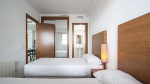 Hotellihuone, jossa on kaksi sänkyä, puinen pääty ja yöpöytälamppu sekä näkymä kylpyhuoneeseen.