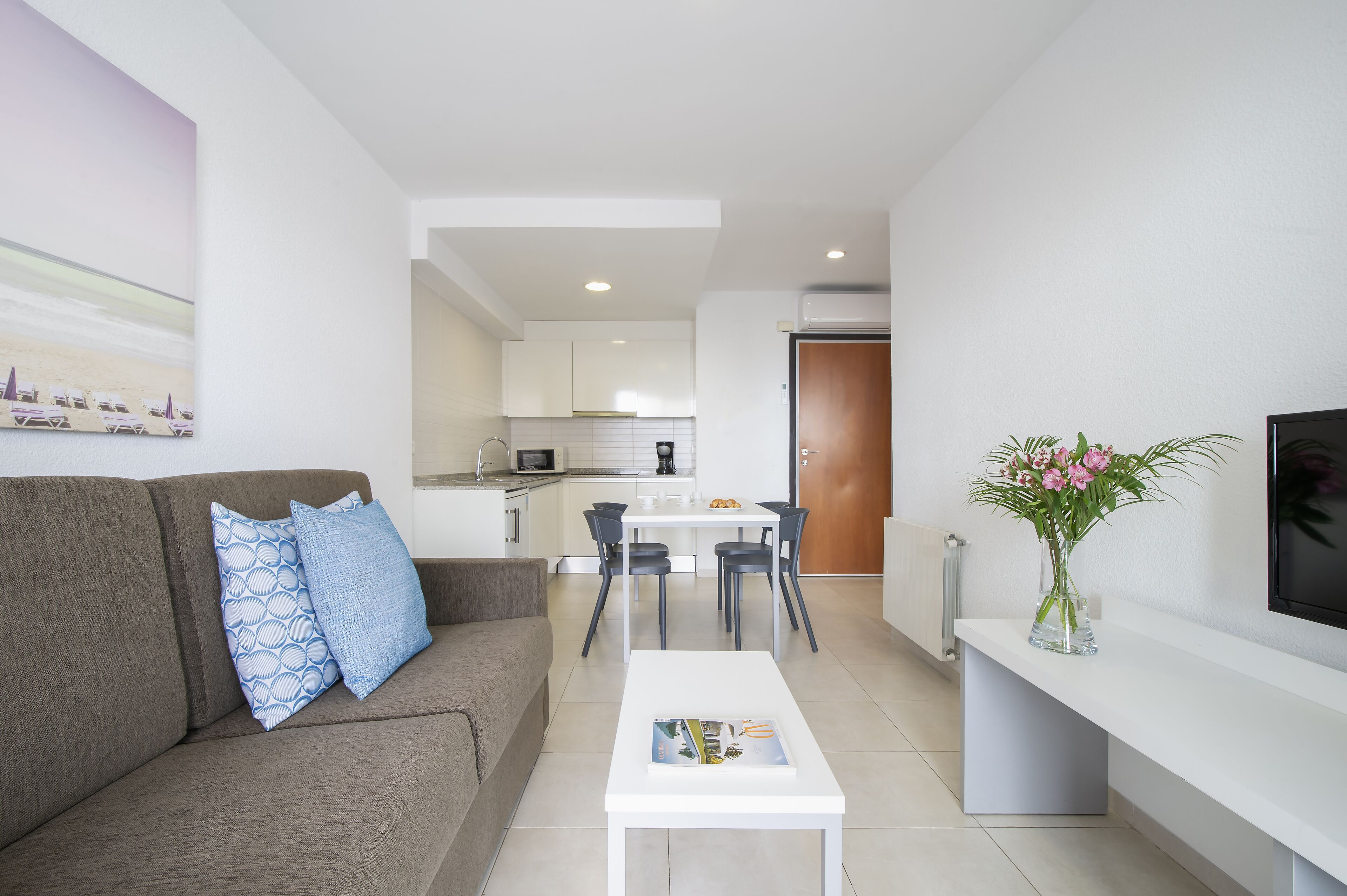 A modern living room with a sofa, coffee table, and a dining area with chairs and a table.