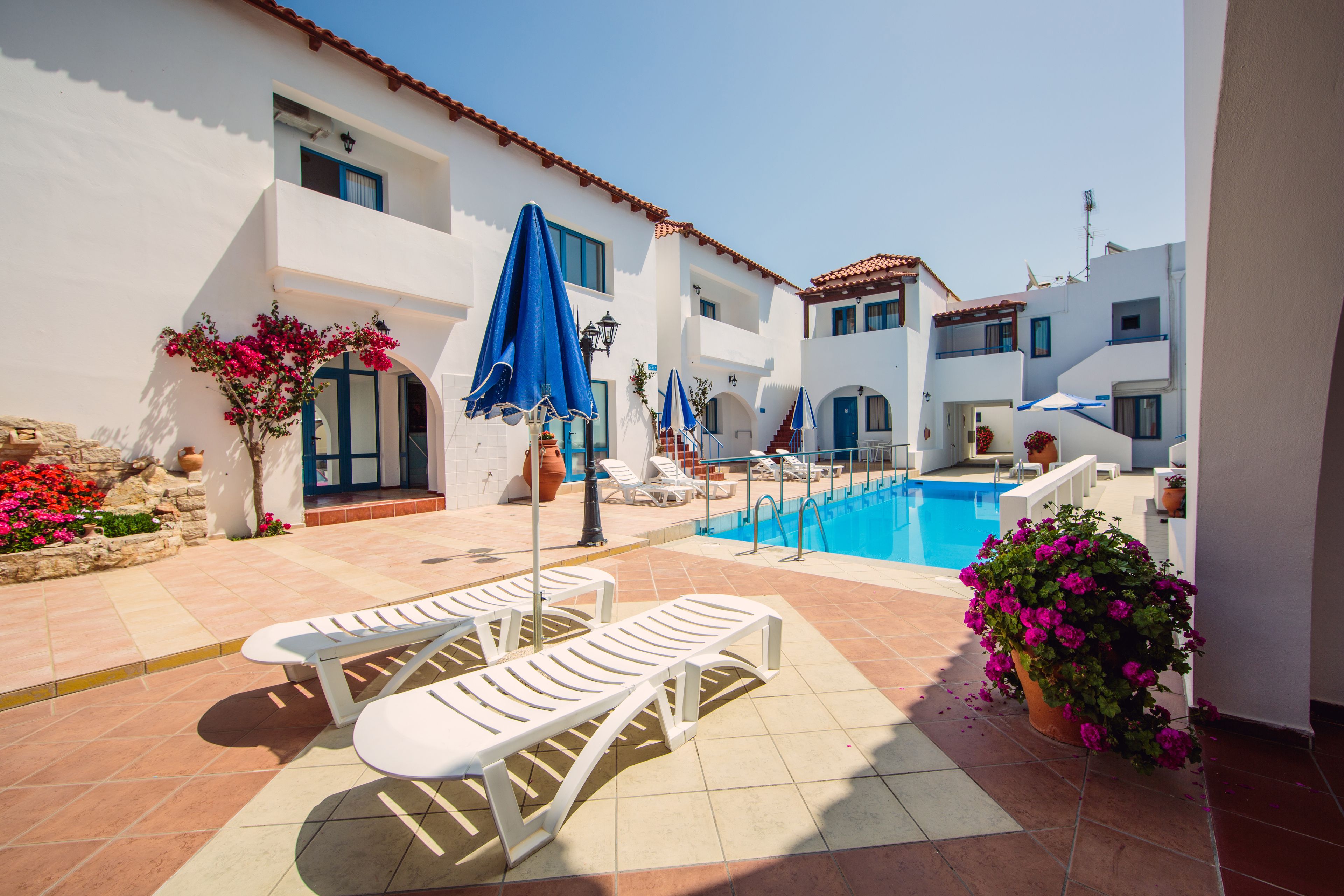 A poolside area with lounge chairs, umbrellas, and potted plants.