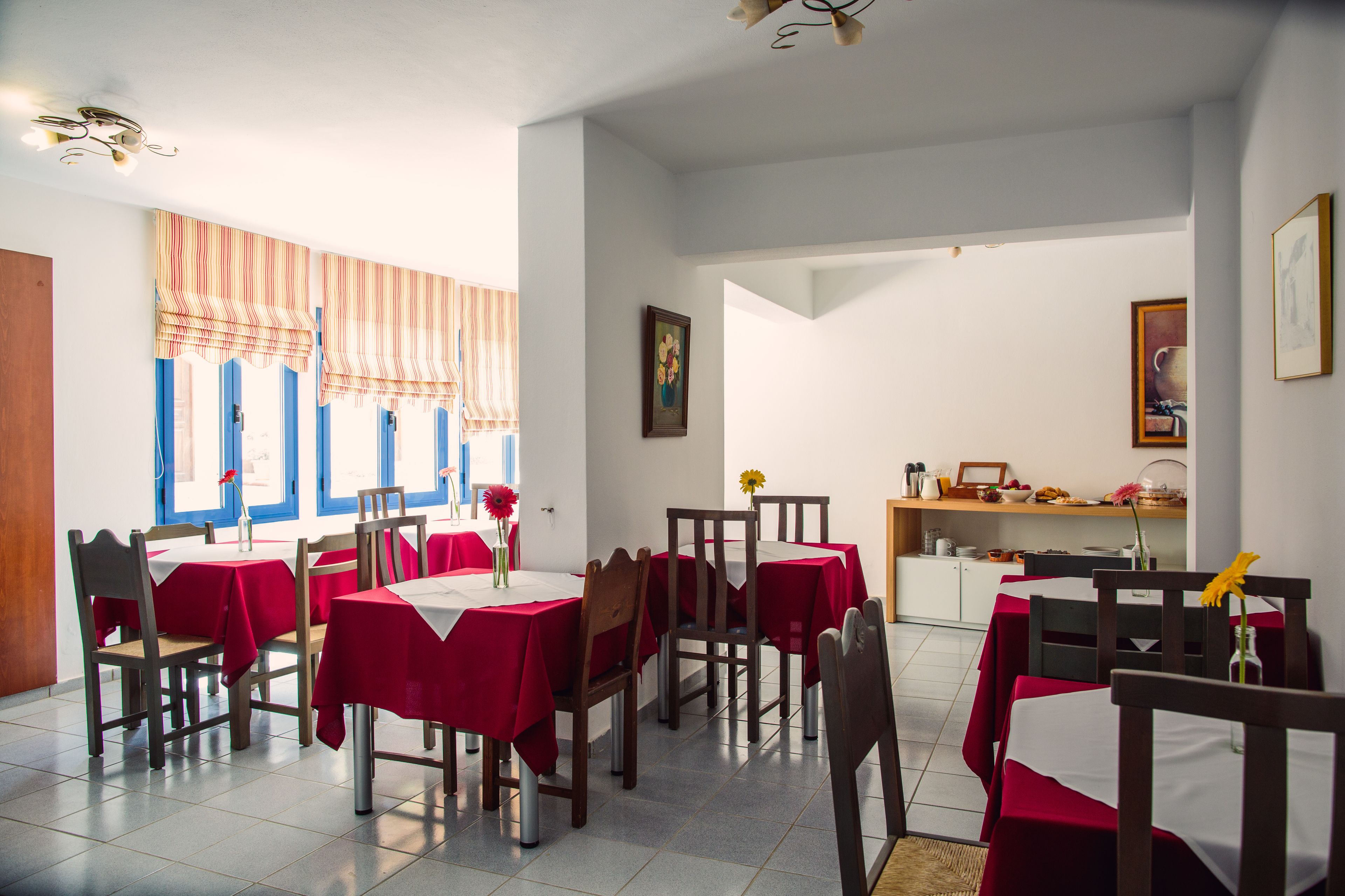 Un espace repas avec des tables dressées pour quatre personnes, des chaises en bois et des nappes rouges.