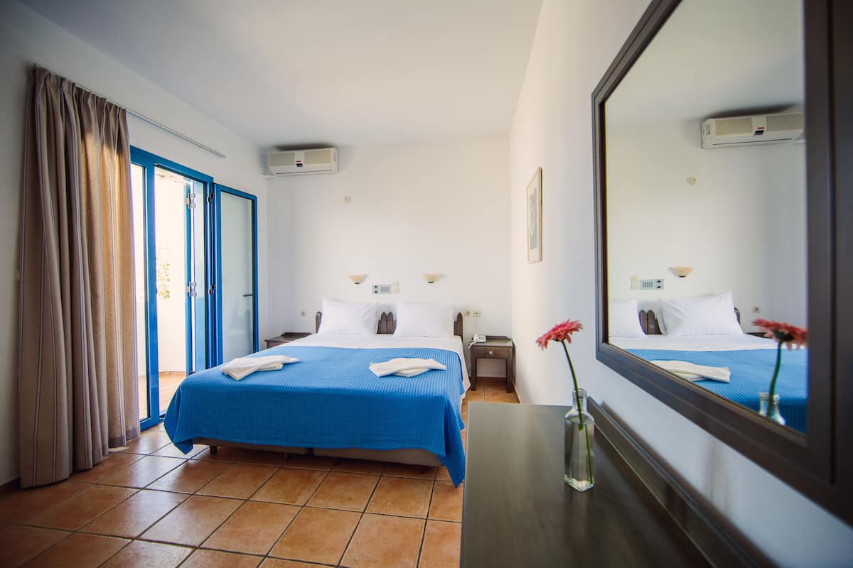 Quarto de hotel com cama grande, mesa de cabeceira, espelho e janela com cortinas.