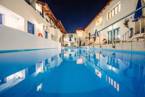 Une piscine à l’eau d’un bleu cristallin, entourée de bâtiments blancs aux portes et fenêtres bleues, et un escalier menant à un niveau supérieur.