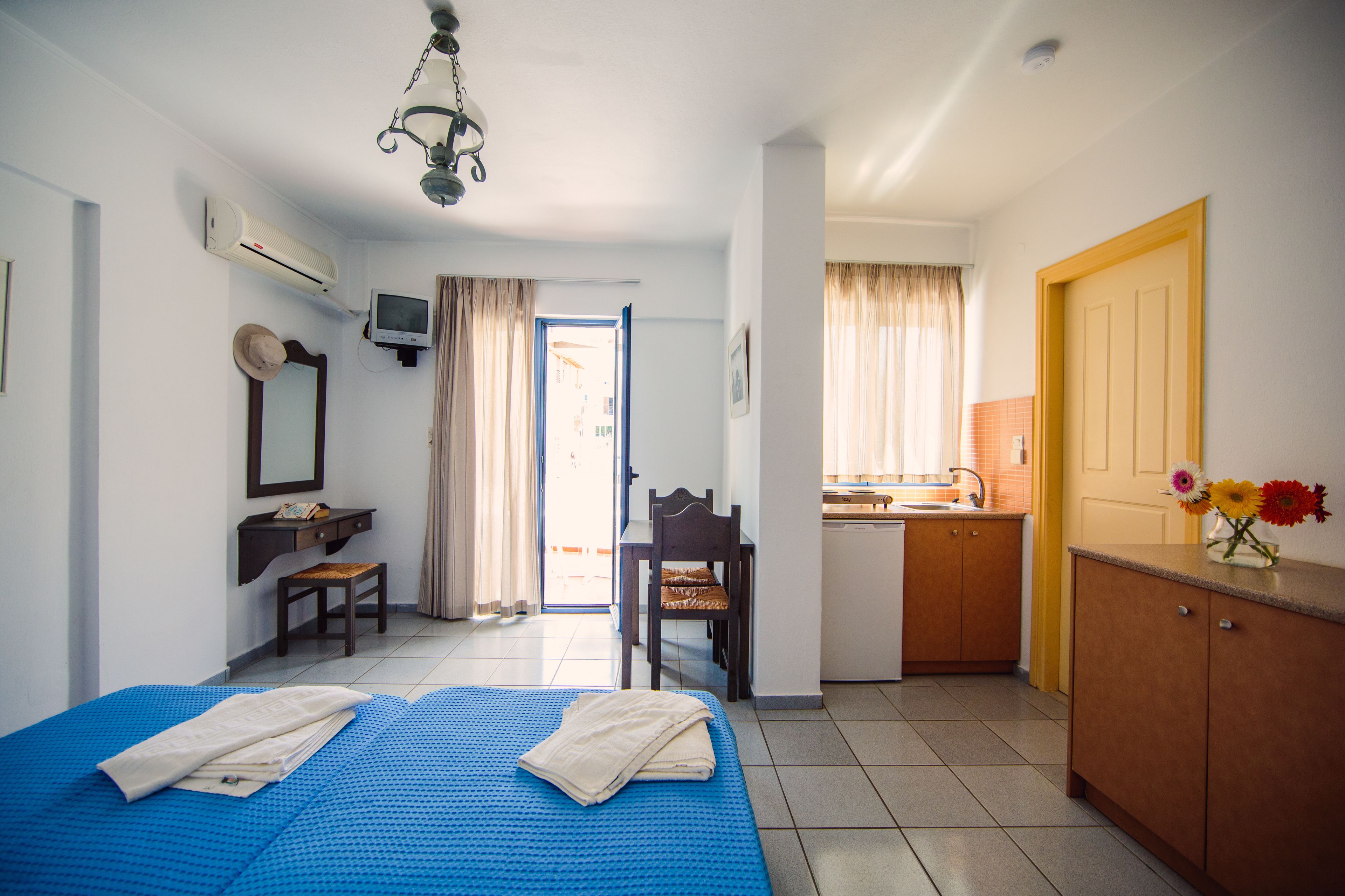 A room with a bed, a desk, a chair, a television, and a kitchenette.