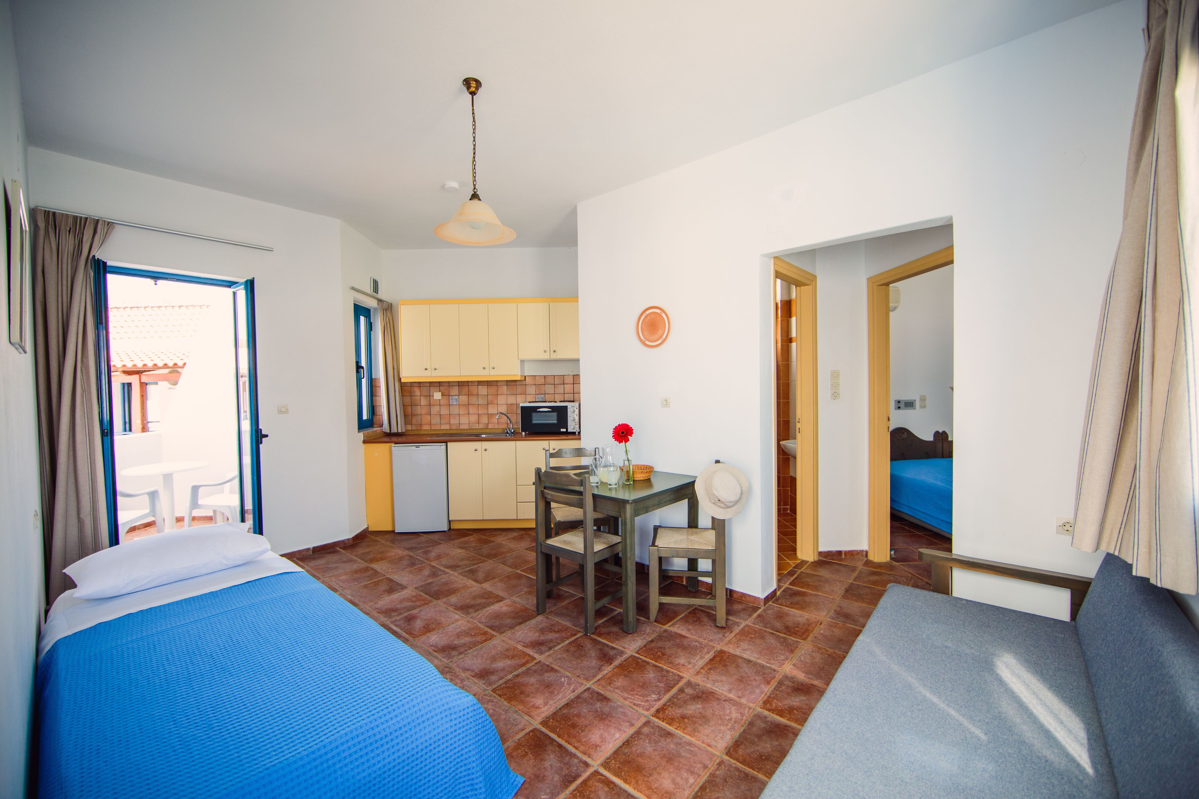 Una camera compatta con un letto, un divano, un piccolo tavolo da pranzo con sedie, angolo cottura e bagno.