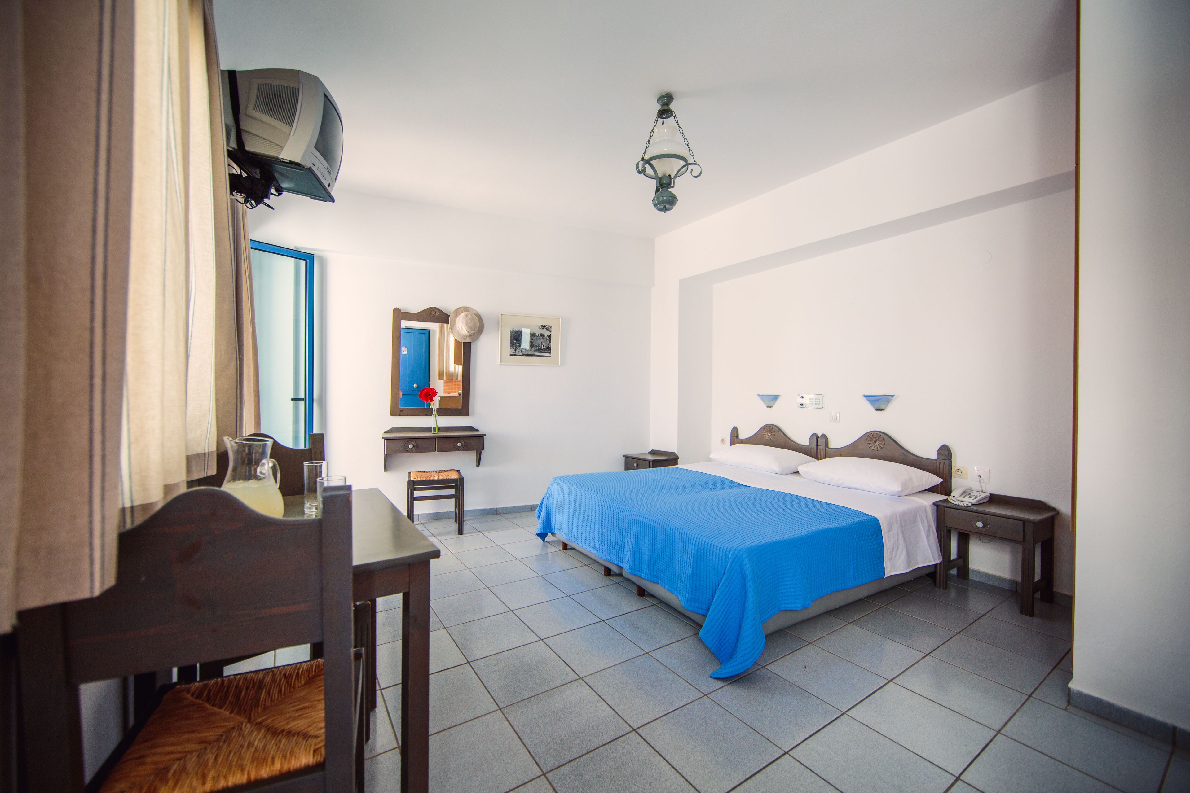 A hotel room with a bed, a desk, a chair, a mirror, and a ceiling fan.