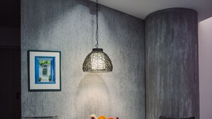 Een eetgedeelte met twee houten stoelen, een kleine ronde tafel, een hanglamp en een ingelijst beeld aan de muur.