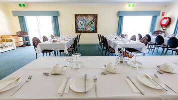 A dining area with tables set for a meal, chairs, and a painting on the wall.