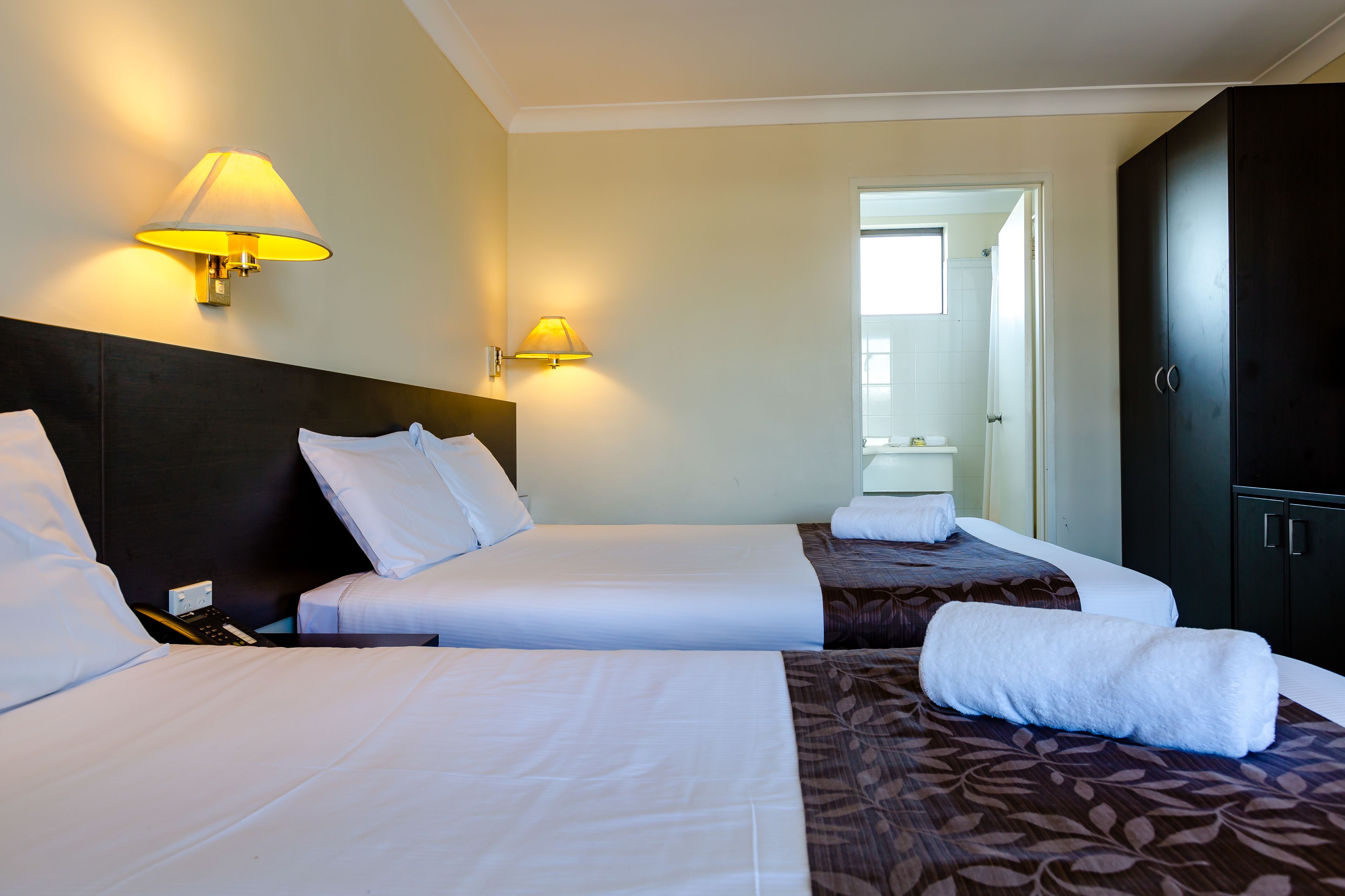 A hotel room with two beds, a dark headboard, and a wardrobe.