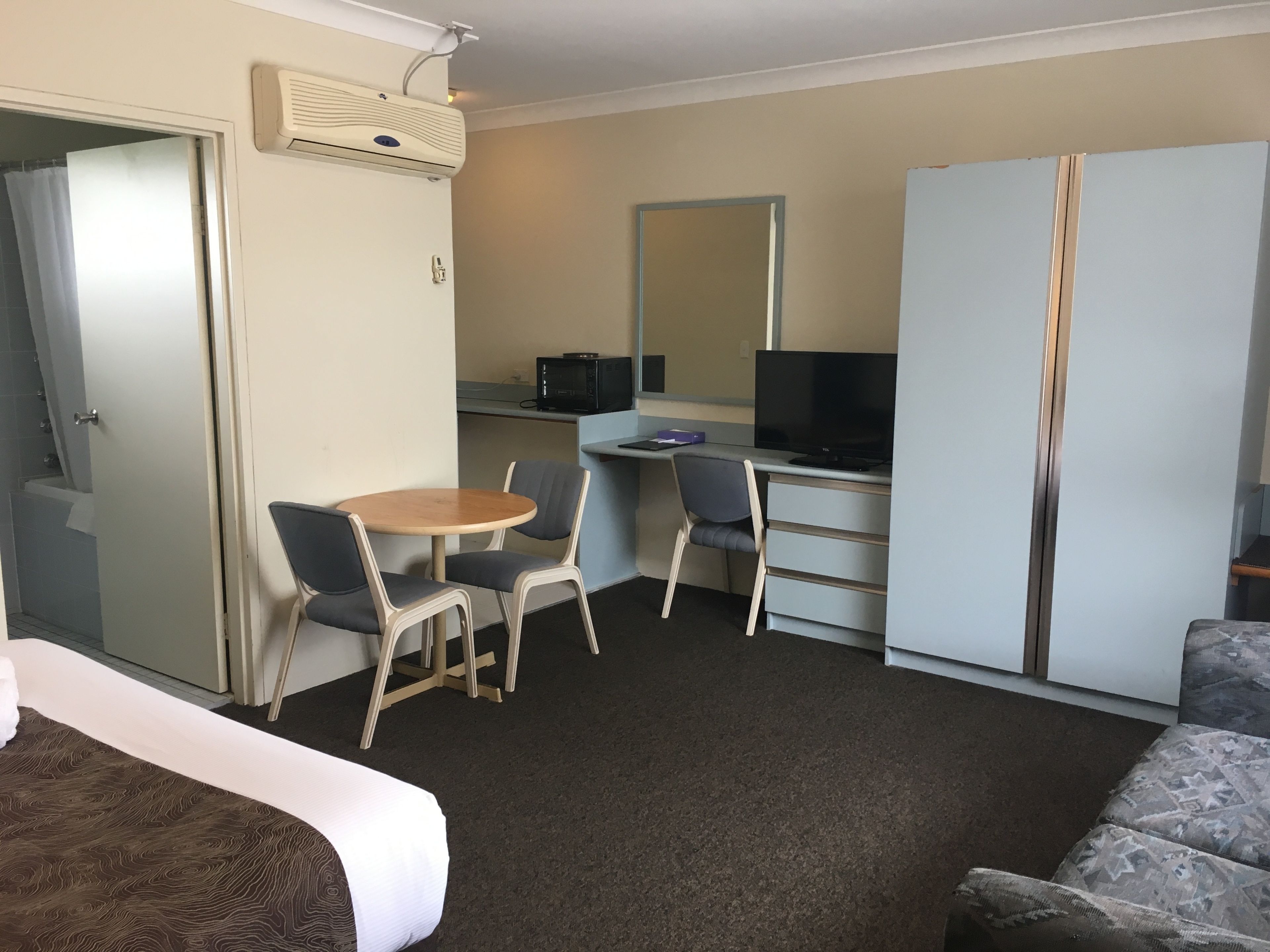 Ein Hotelzimmer mit Bett, Schreibtisch mit Computer und Fernseher, Stuhl, kleinem Tisch und Kleiderschrank.