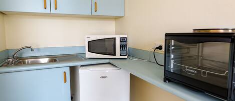 A compact kitchenette with a white microwave, a small refrigerator, and a black oven.