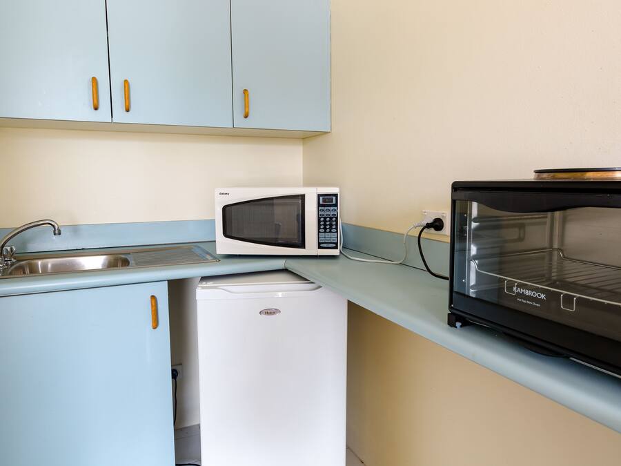 A compact kitchenette with a white microwave, a small refrigerator, and a black oven.