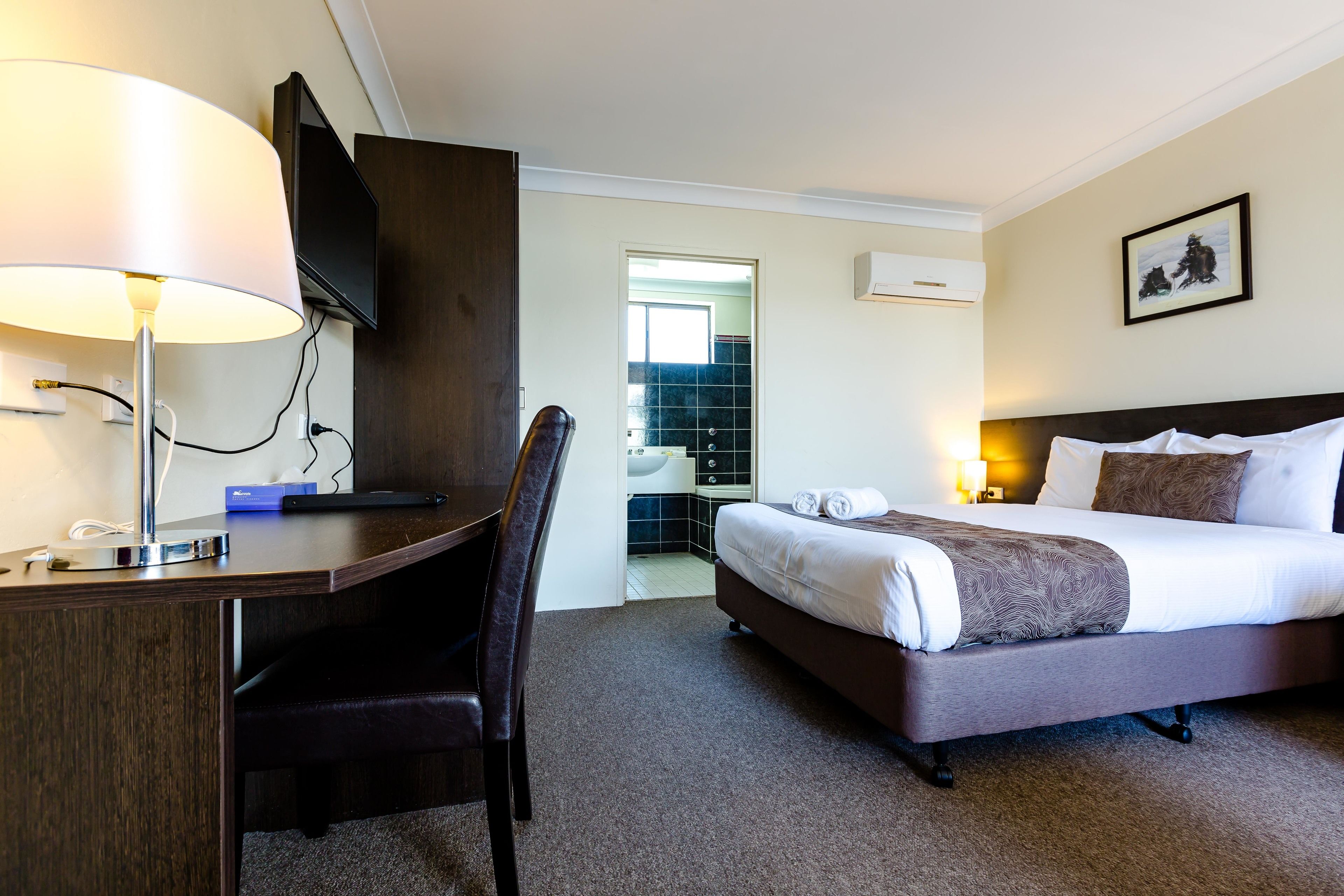 A hotel room with a desk, chair, bed, and a bathroom visible through an open door.