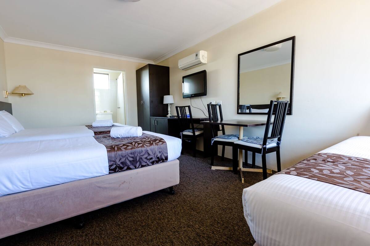 Quarto de hotel com duas camas, uma escrivaninha, uma cadeira, uma televisão e um espelho.