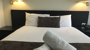 A neatly made bed with white and brown pillows, a rolled white towel, and a dark brown patterned bedspread.