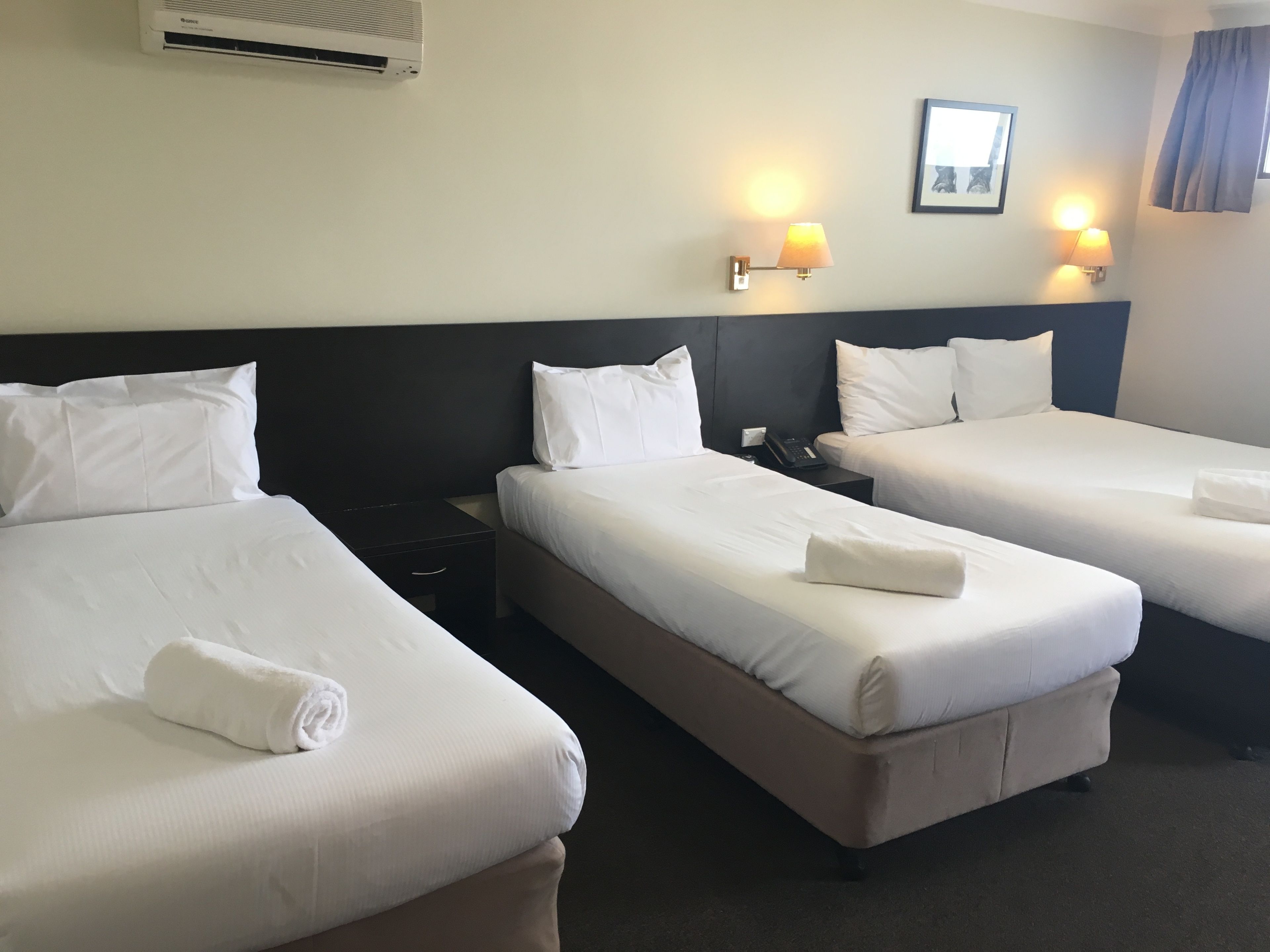 Een hotelkamer met drie bedden, een nachtkastje, een lamp en een airconditioner.