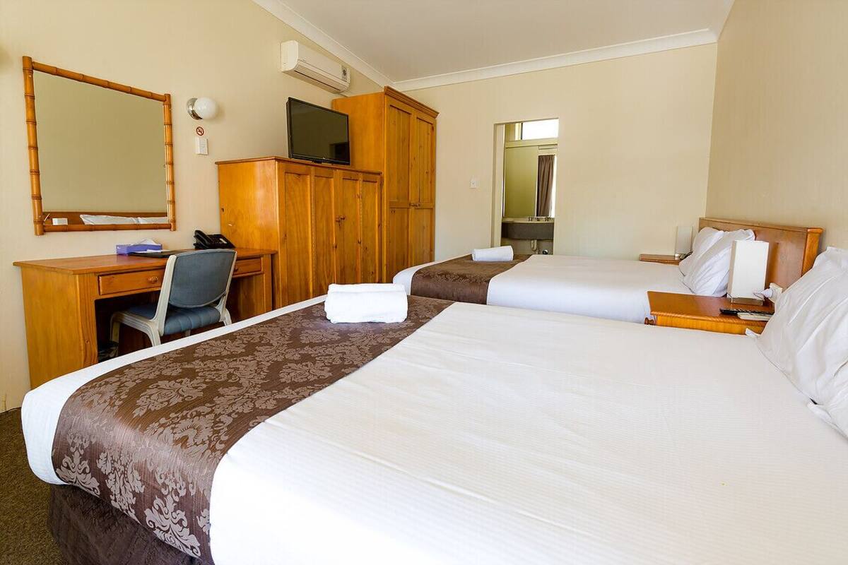 Quarto de hotel com duas camas, uma escrivaninha, uma cadeira, uma televisão e um espelho.