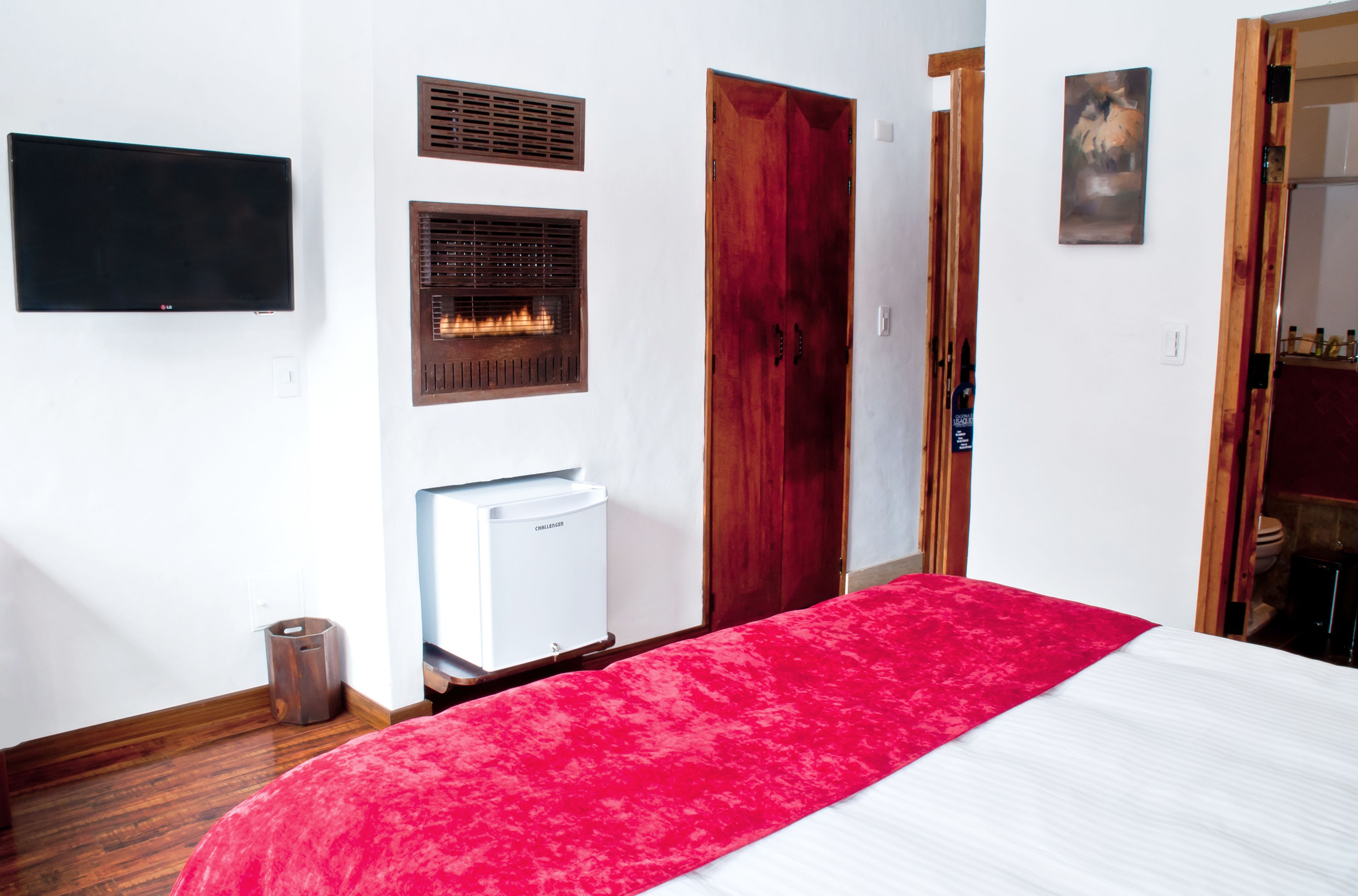 A hotel room with a bed, a TV mounted on the wall, a fireplace, and a wooden door.