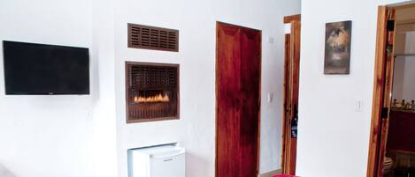 A hotel room with a bed, a TV mounted on the wall, a fireplace, and a wooden door.