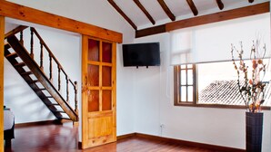 A spacious room with wooden flooring, a wooden staircase, a large window, and a flat-screen TV mounted on the wall. - Hotel Casona de Usaquén (Bogotá)