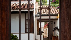 A courtyard with a tiled roof, a wooden door with metal bars, and potted plants. - Hotel Casona de Usaquén (Bogotá)
