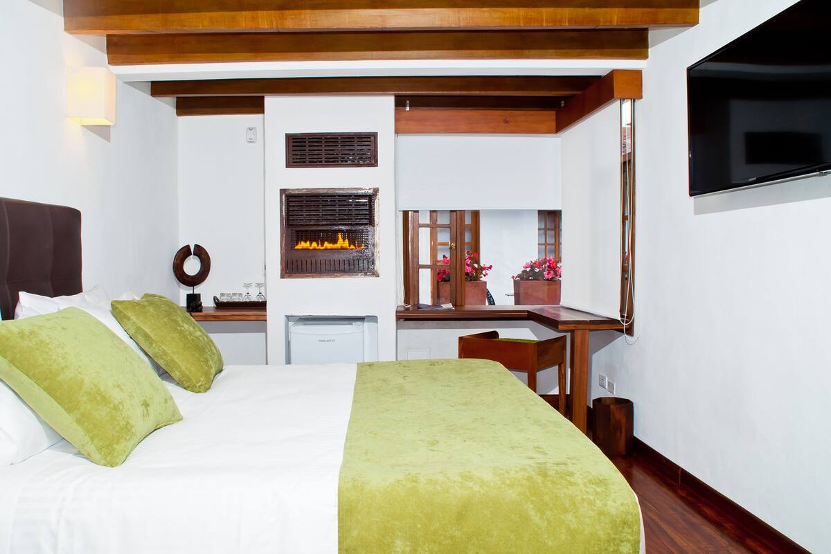 A hotel room with a bed, a desk with a computer, a TV mounted on the wall, and a fireplace.