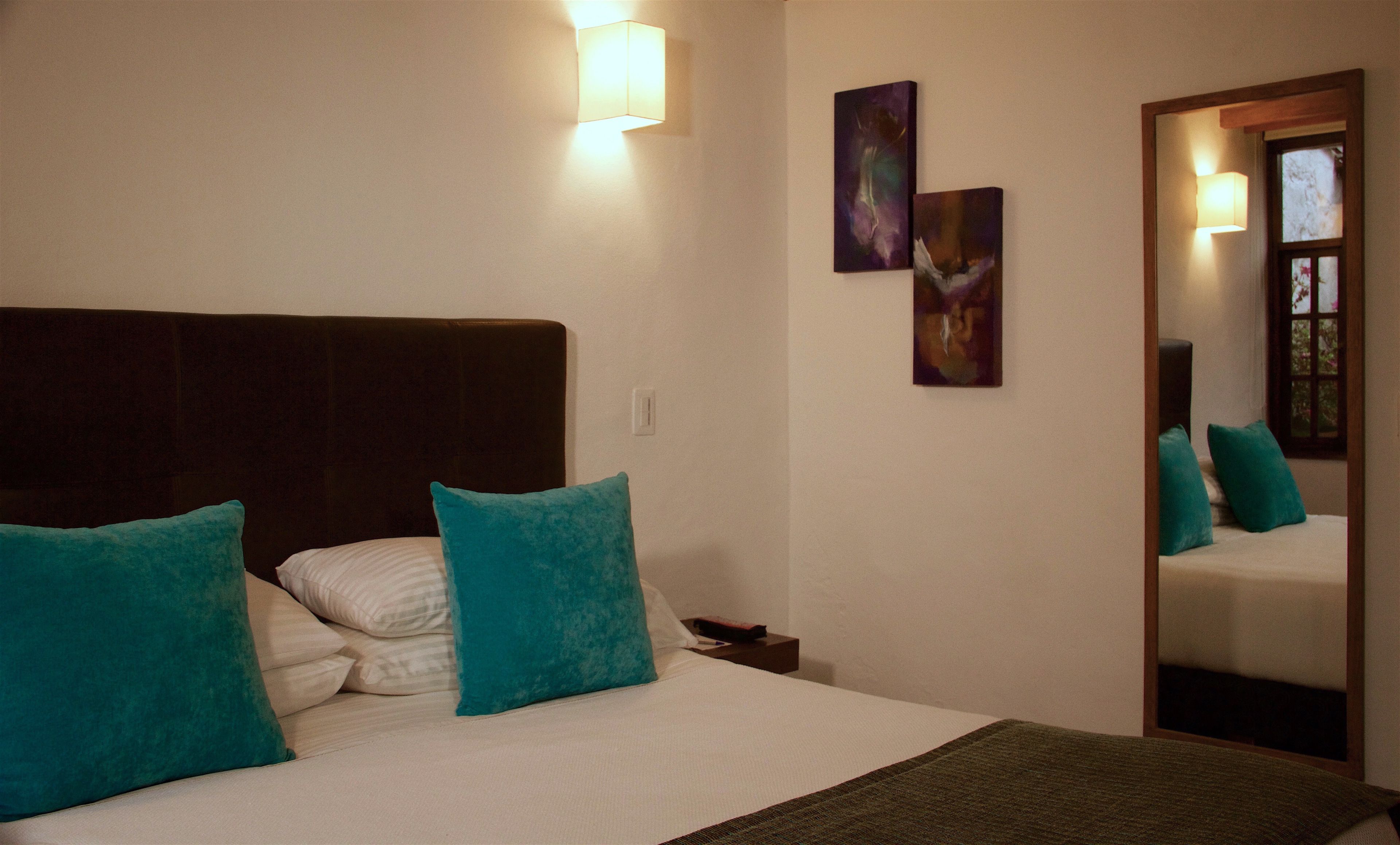 A bedroom with a large bed, two teal pillows, a dark headboard, and two wall-mounted light fixtures.
