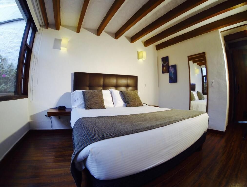 Un dormitorio con una cama grande, vigas de madera en el techo, una mesita de noche y una ventana.