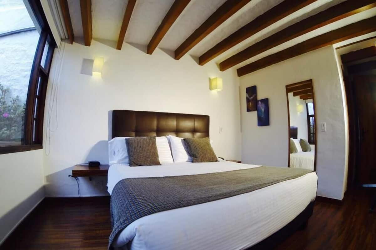 A bedroom with a large bed, wooden beams on the ceiling, a nightstand, and a window.