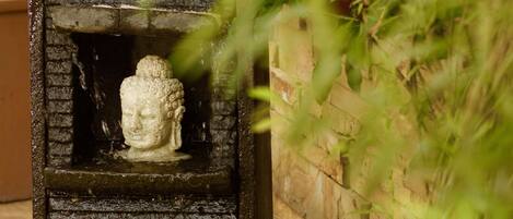A stone water feature with a Buddha statue, surrounded by greenery.