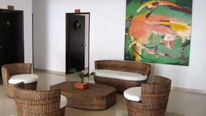 Una habitación con muebles de mimbre, una puerta adornada con un arreglo floral y un cuadro abstracto de colores en la pared.