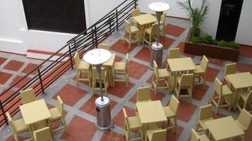 A spacious outdoor seating area with multiple tables and chairs, a metal trash can, and a staircase with a black railing.