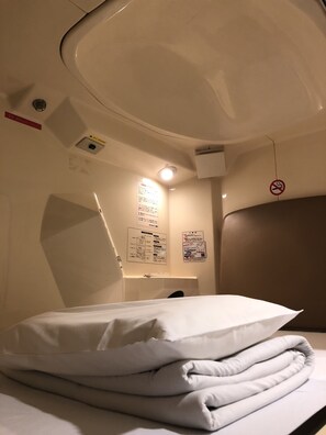 A hotel room with a neatly made bed, a wall-mounted information board, and a no-smoking sign. - Capsule Inn Kamata (Tokyo)