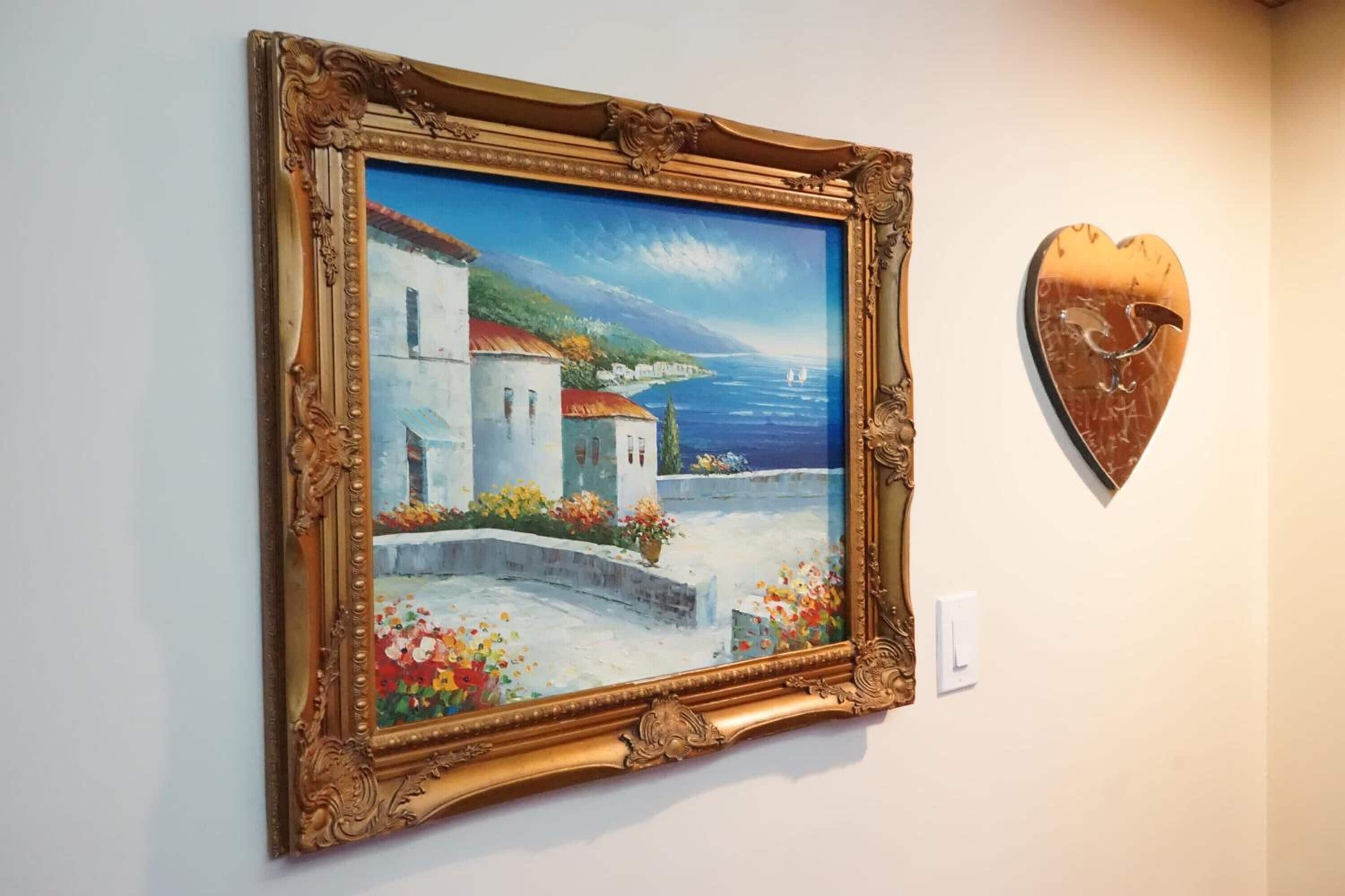Ein gerahmtes Gemälde einer Küstenlandschaft mit herzförmiger Dekoration an der Wand.