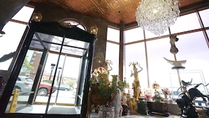 A lobby with a large chandelier, a glass door entrance, and various statues and vases. - Paris Suites Hotel (Corona)