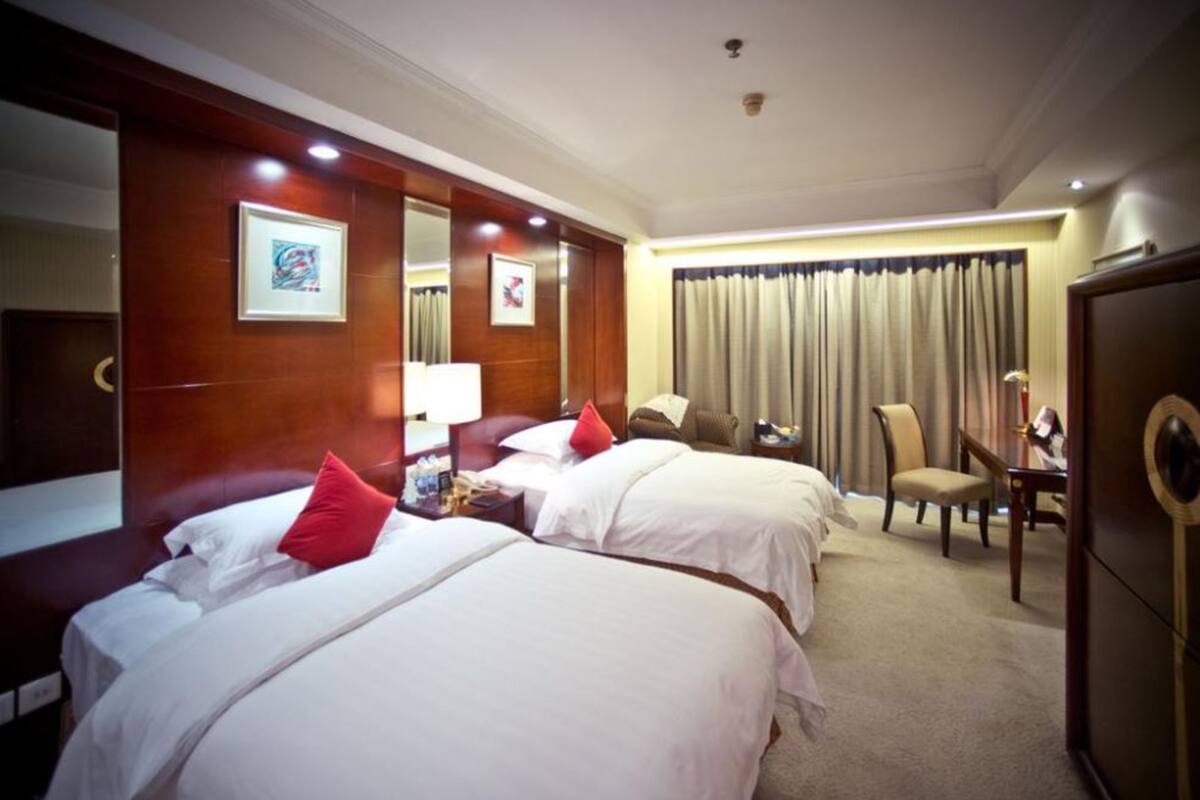 A hotel room with two beds, a desk, a chair, a wardrobe, and a large window with curtains.