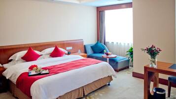 Habitació d'hotel amb un llit gran, una taula petita, una cadira i una finestra amb cortines.